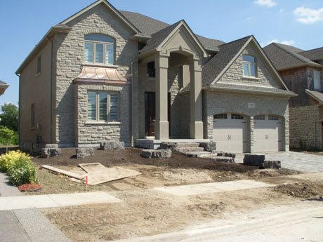 We added a flower bed that helped balance the landscape because the driveway was visually heavy on the right side of the house so we balanced out with a larger flower bed on the opposite side. We tied the stone in from the driveway and the steps by placing armour stone in the bed as well. The shape of the bed allows for easier lawn cutting as now you do not have to cut right up against the stones of the steps.